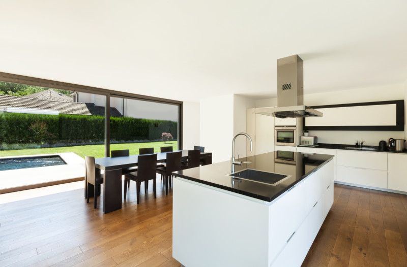 Modern villa interior with beautiful white kitchen, long island with tap and sink, dining table and timber floor bespoke kitchen island designs